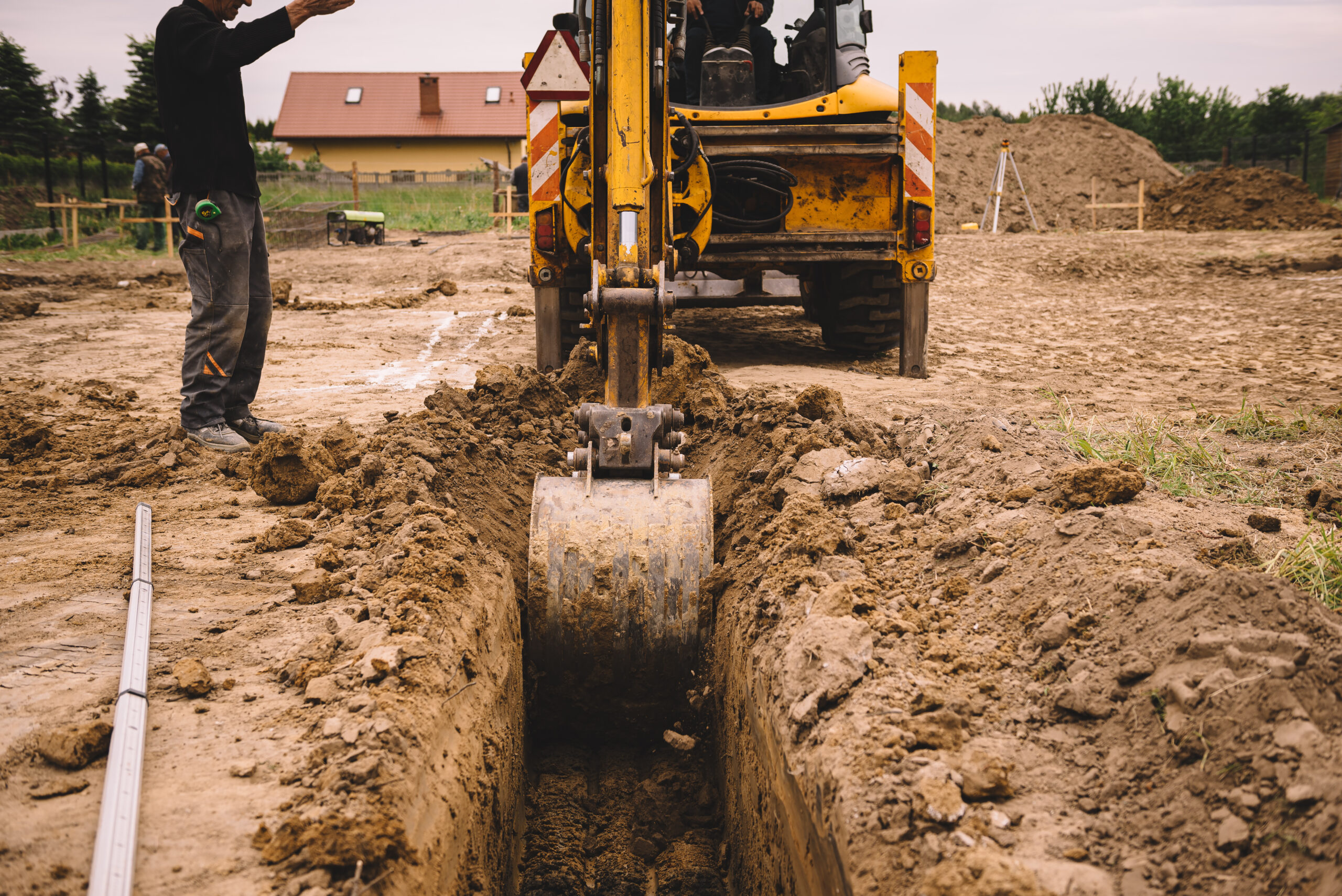 Excavator working at house construction site - digging foundations for modern house. Beginning of house building. Earth moving and foundation preparation.