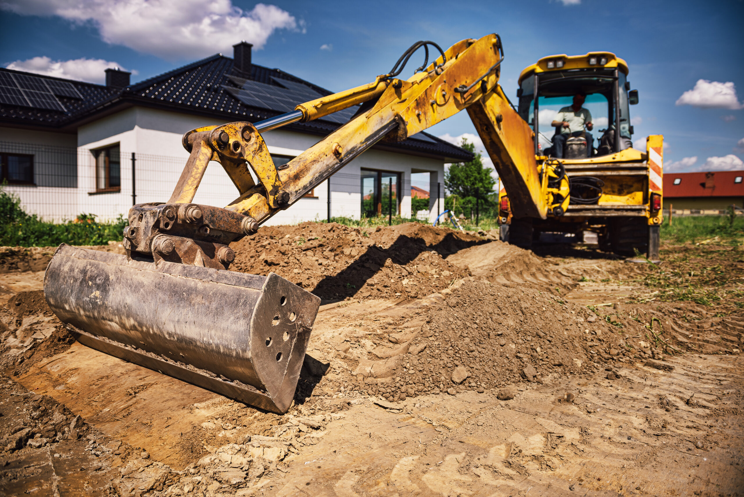 Excavator working at house construction site - digging foundations for modern house. Beginning of house building. Earth moving and foundation preparation.